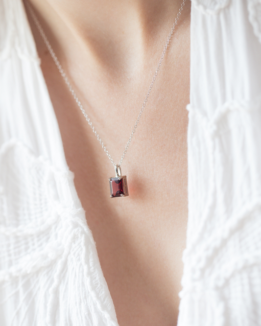Necklace with a square garnet gemstone pendant on a person wearing a white garment