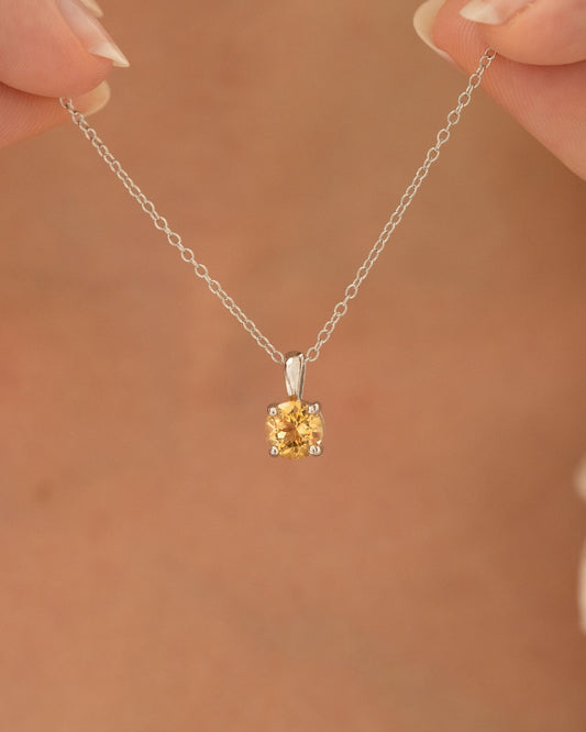Silver necklace with a round citrine pendant held by hands against a brown background