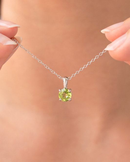 Silver necklace with a green peridot gemstone held by hands against a blurred background