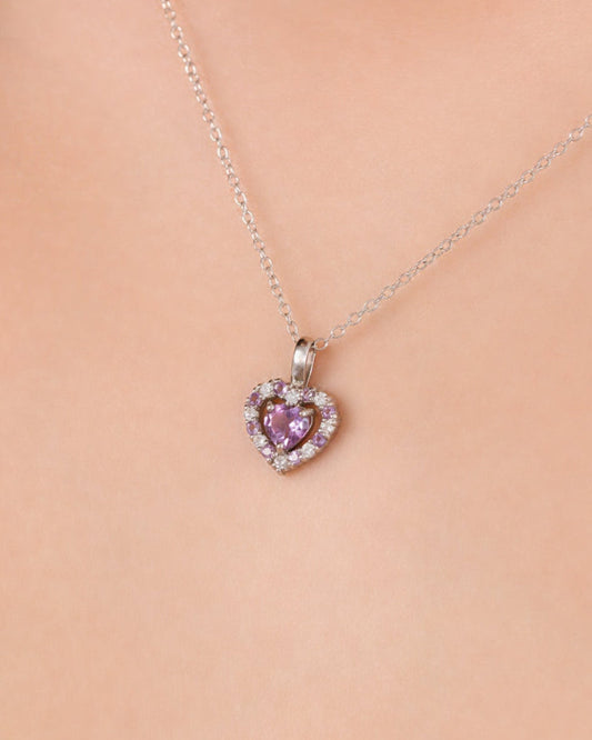 Heart-shaped pendant with amethyst gemstone on a chain against a beige background