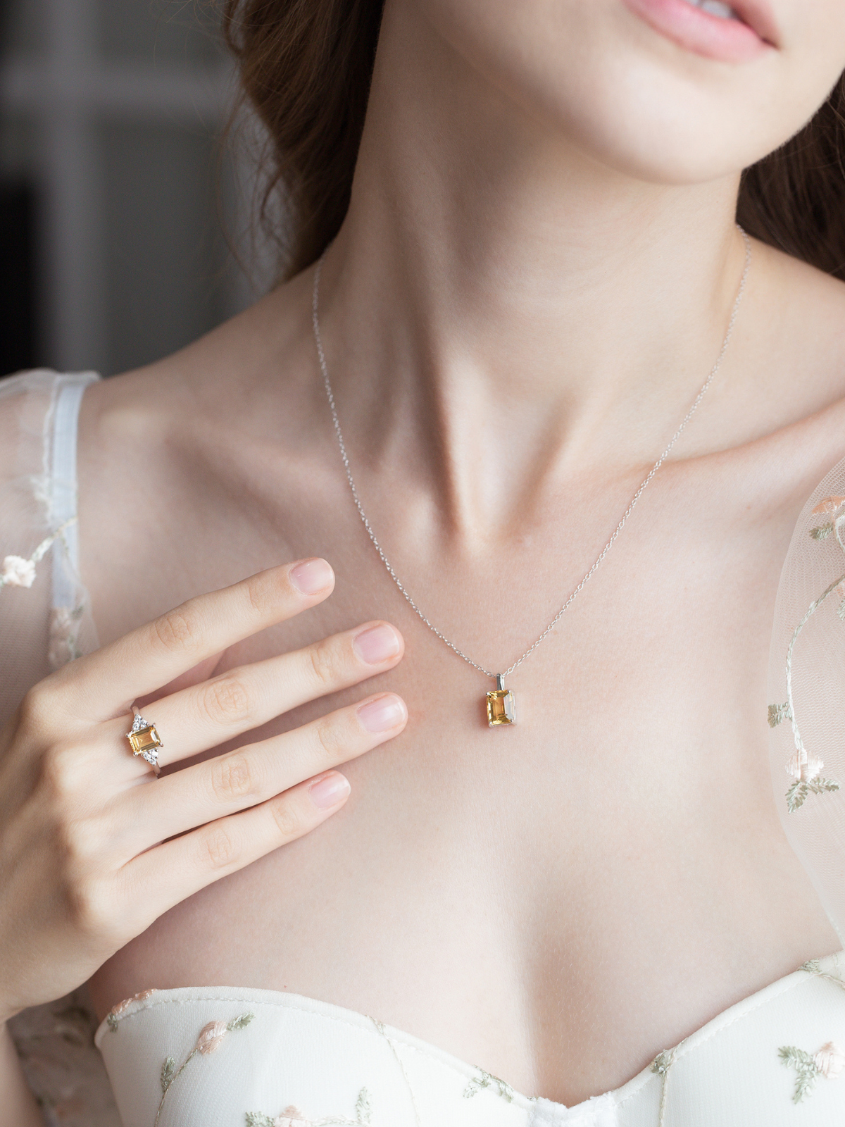 Woman wearing a silver citrine necklace and ring, with a blurred background