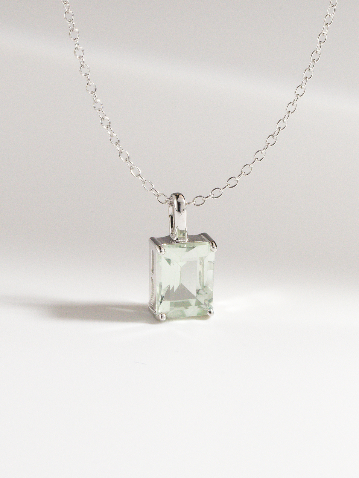 Silver necklace with a square green amethyst gemstone pendant on a light gray background