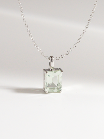 Silver necklace with a square green amethyst gemstone pendant on a light gray background