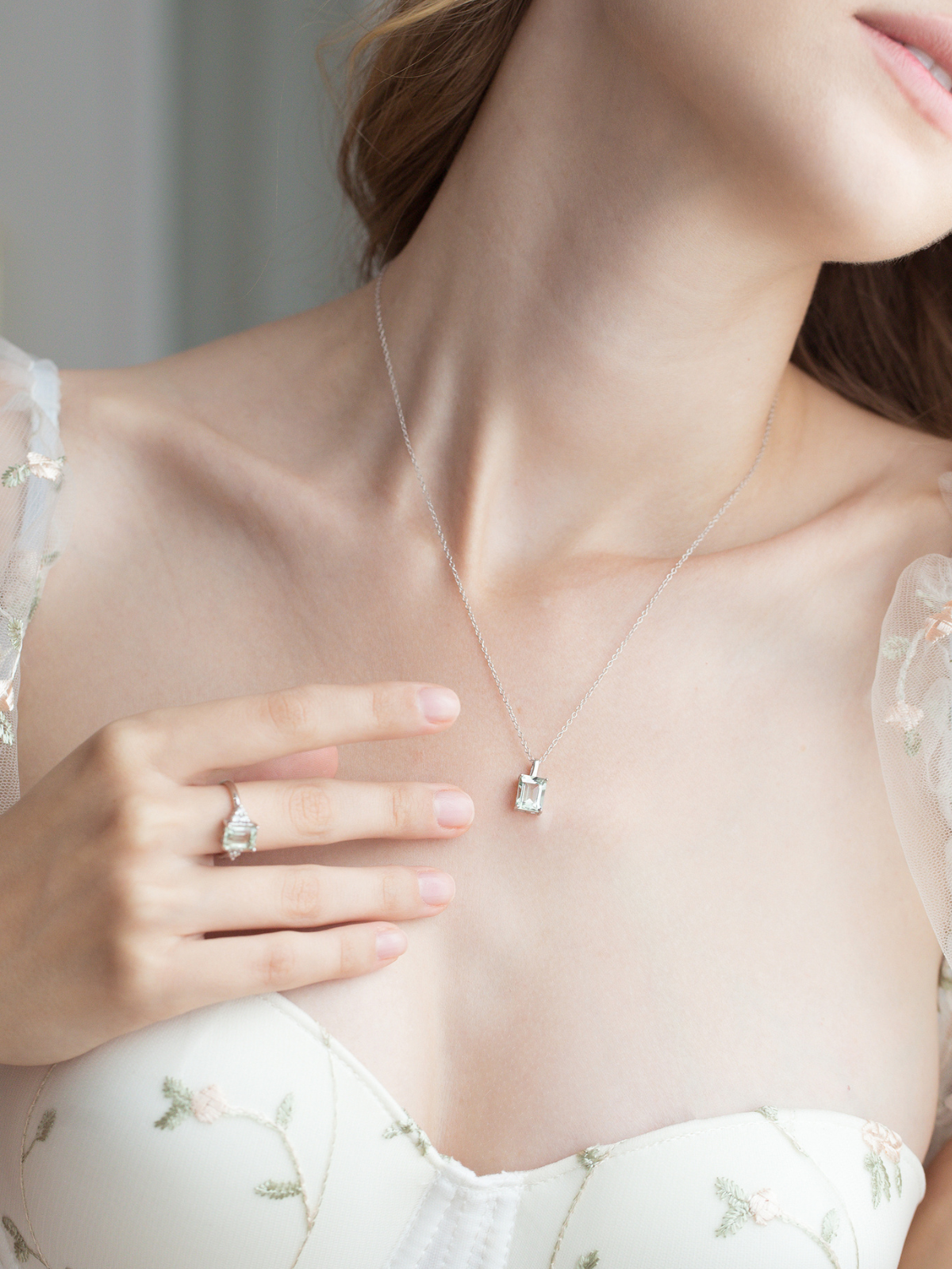 Close-up of a silver necklace with a green amethyst pendant worn by a person, with a soft focus on the background.