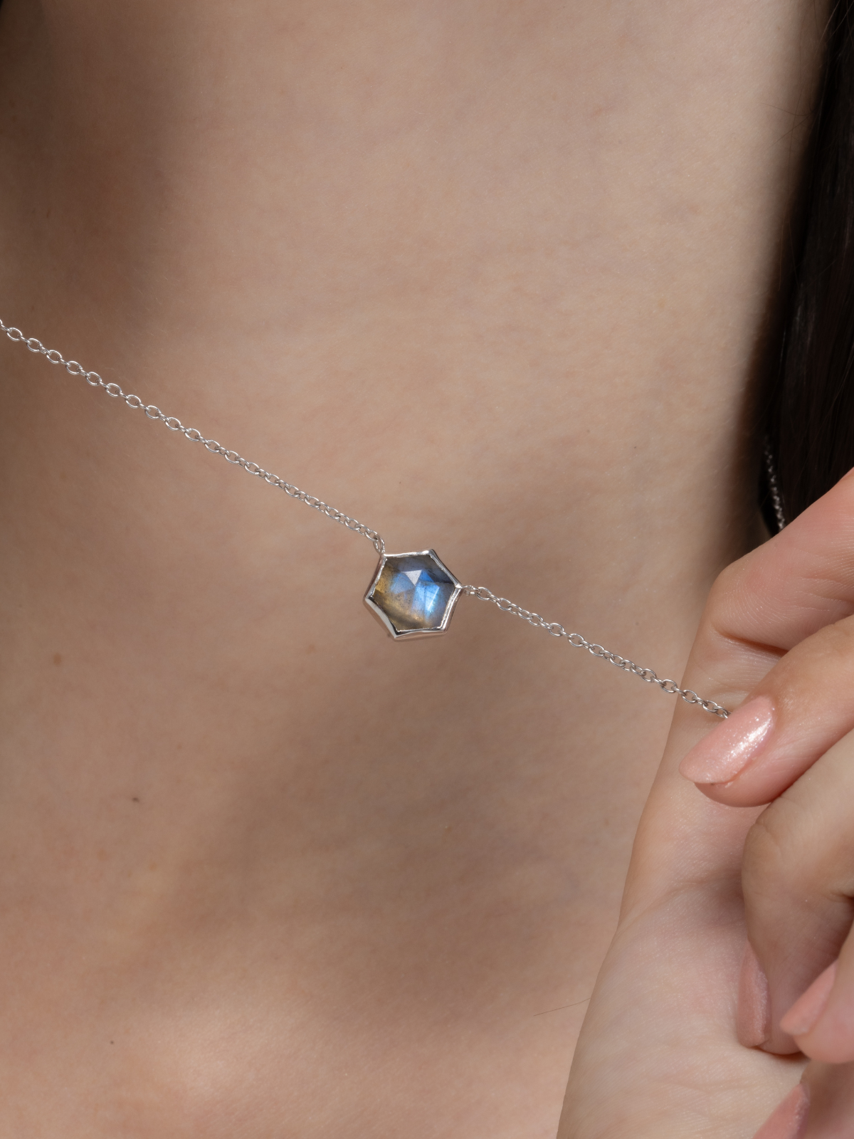 Silver necklace with a hexagonal labradorite gemstone worn by a woman