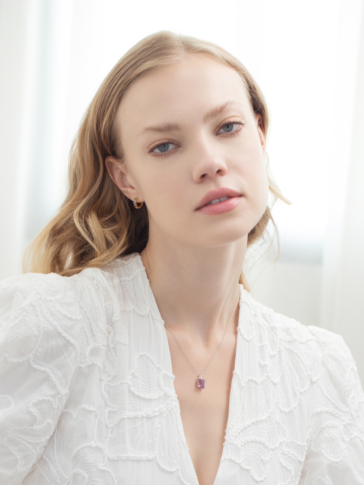 Woman wearing a white textured top with an amethyst necklace against a light background