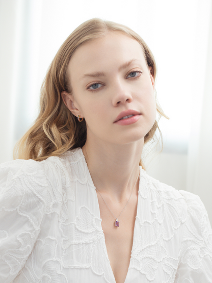 Woman wearing a white textured top with an amethyst necklace against a light background