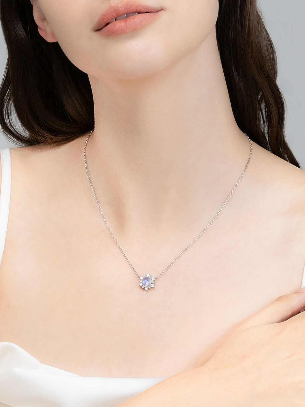 Necklace with a moonstone pendant worn by a person against a neutral background