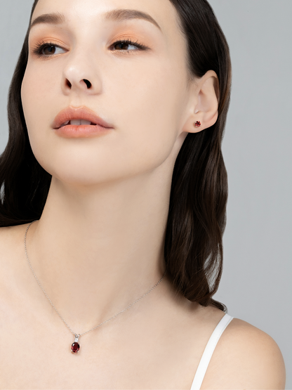 Woman wearing a necklace with a garnet pendant on a plain background