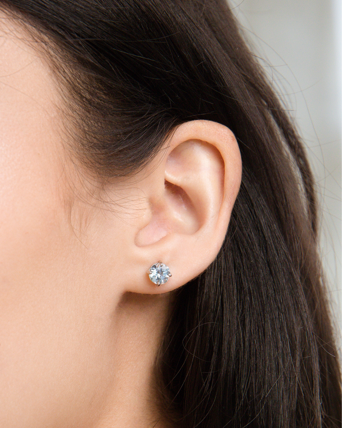 Close-up of an ear wearing a blue topaz stud earring with blurred background