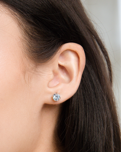 Close-up of an ear wearing a blue topaz stud earring with blurred background