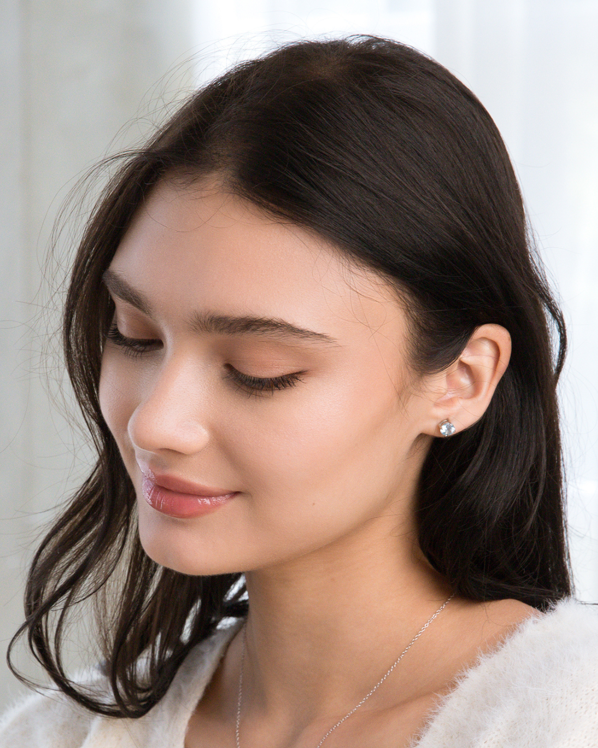 Close-up of a woman wearing blue topaz earrings with a plain background