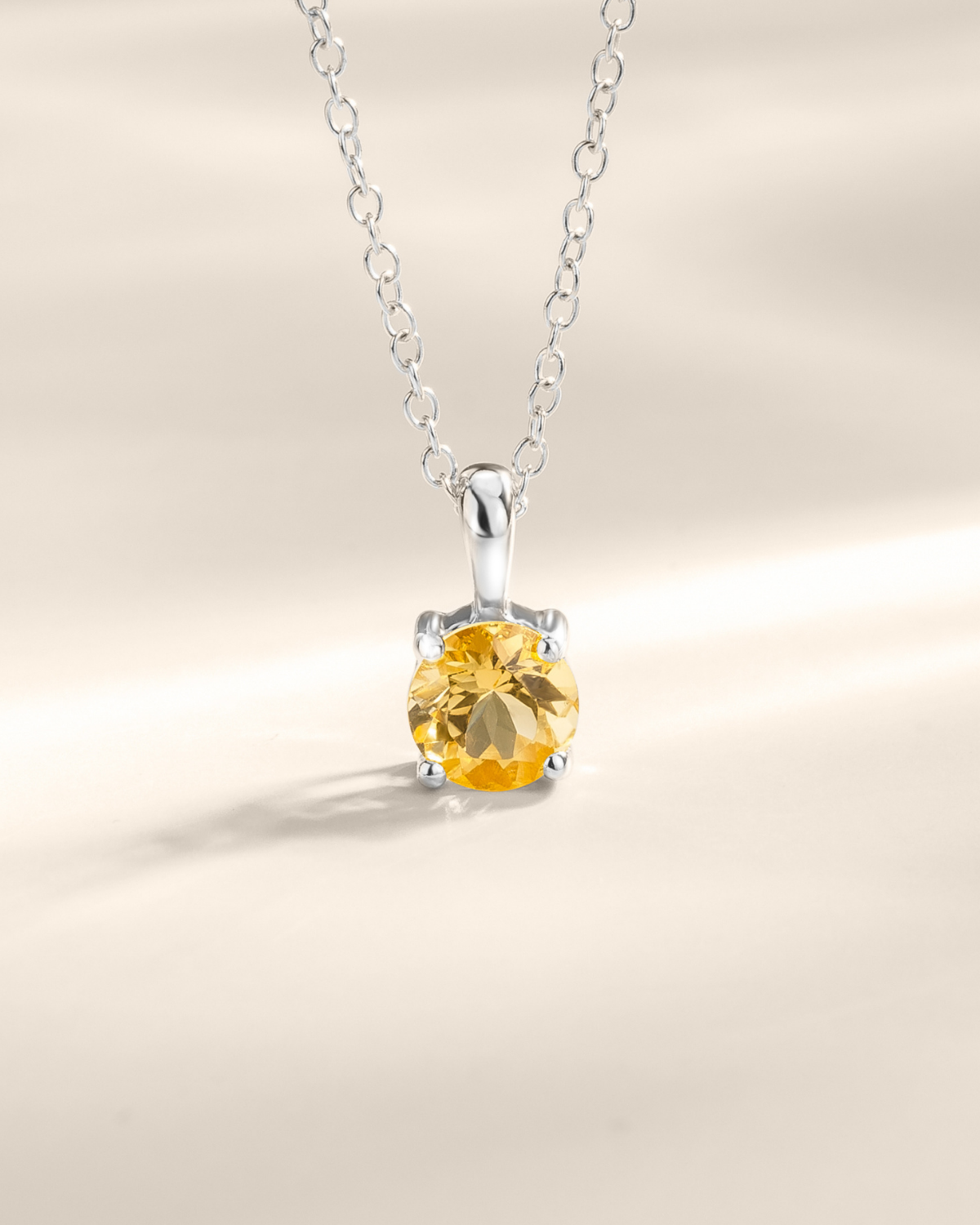 Silver necklace with a yellow citrine gemstone pendant on a neutral background