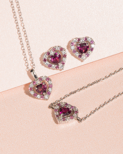 Heart-shaped jewellery set with red garnet gemstones on a pink background