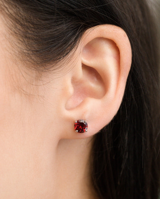 Close-up of an ear wearing a red garnet gemstone stud earring with blurred background