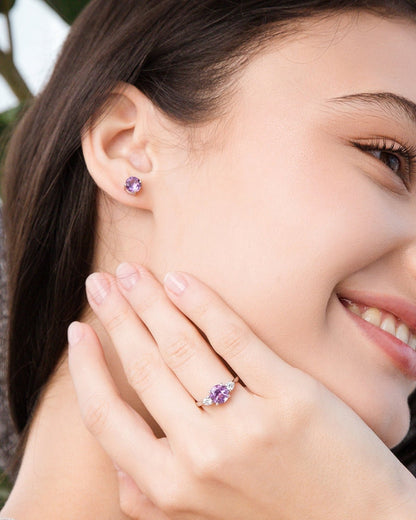 Woman wearing purple amethsyt silver earrings and ring, smiling outdoors.