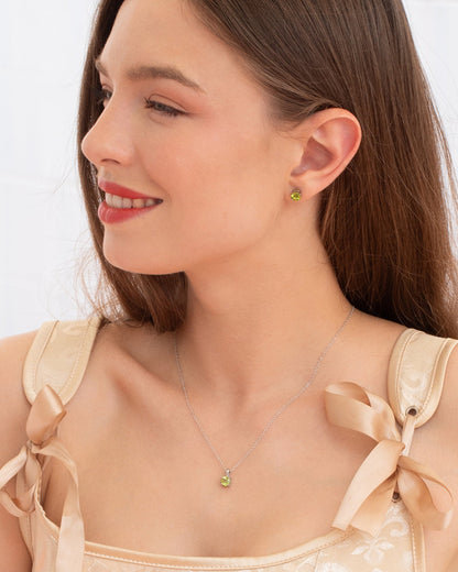 Woman wearing a peridot necklace and earrings with a plain background