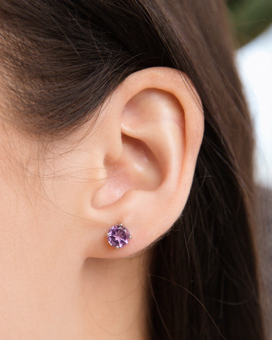 Close-up of an ear wearing a purple amethyst stud earring with a blurred background