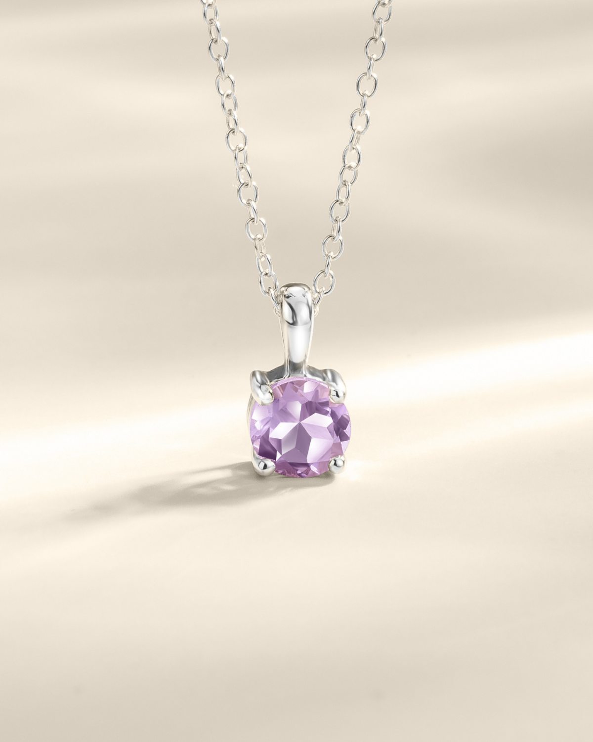 Silver necklace with a purple amethyst gemstone pendant on a beige background