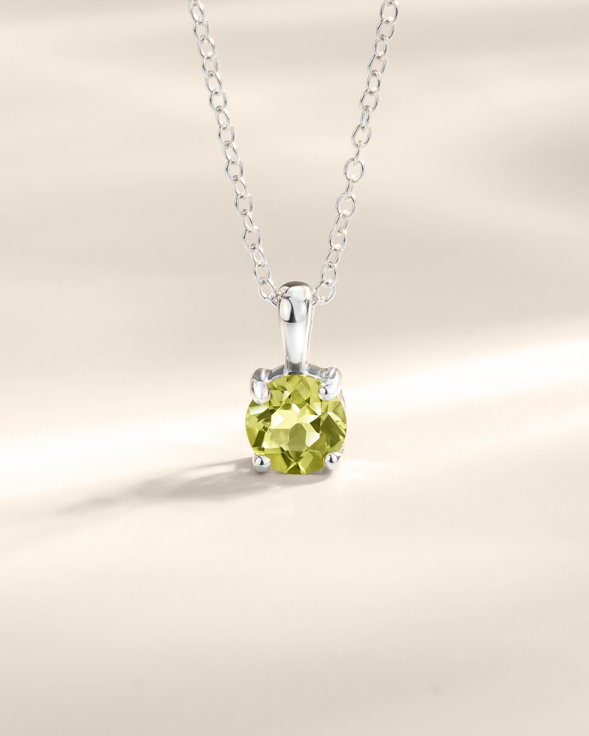Silver necklace with a green peridot gemstone pendant on a beige background
