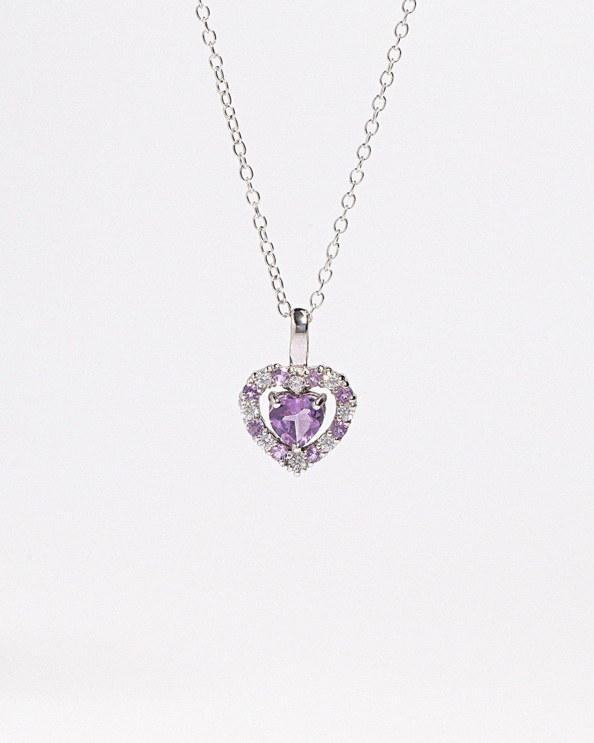 Heart-shaped purple amethyst gemstone pendant on a chain against a white background