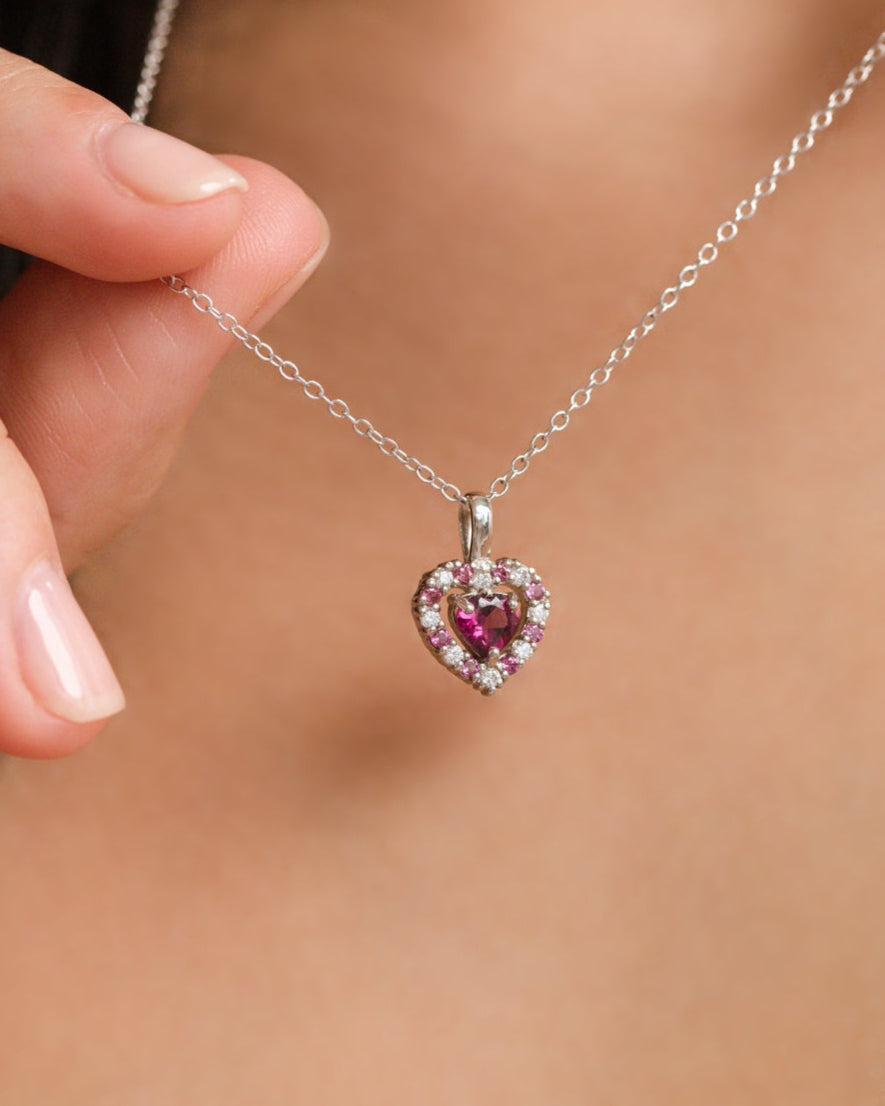 Heart-shaped pendant necklace with a pink garnet gemstone held by a hand against a blurred background