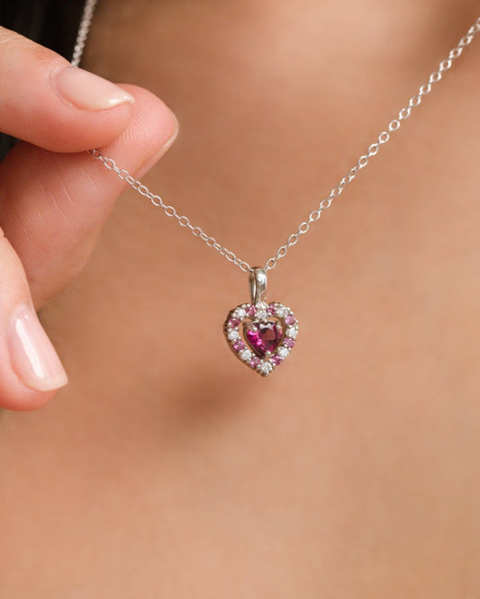 Heart-shaped pendant necklace with a pink garnet gemstone held by a hand against a blurred background
