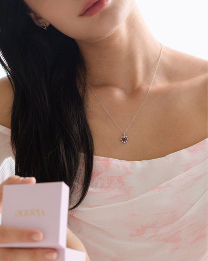 Woman wearing a delicate necklace with a small garnet pendant, holding a white gift box.