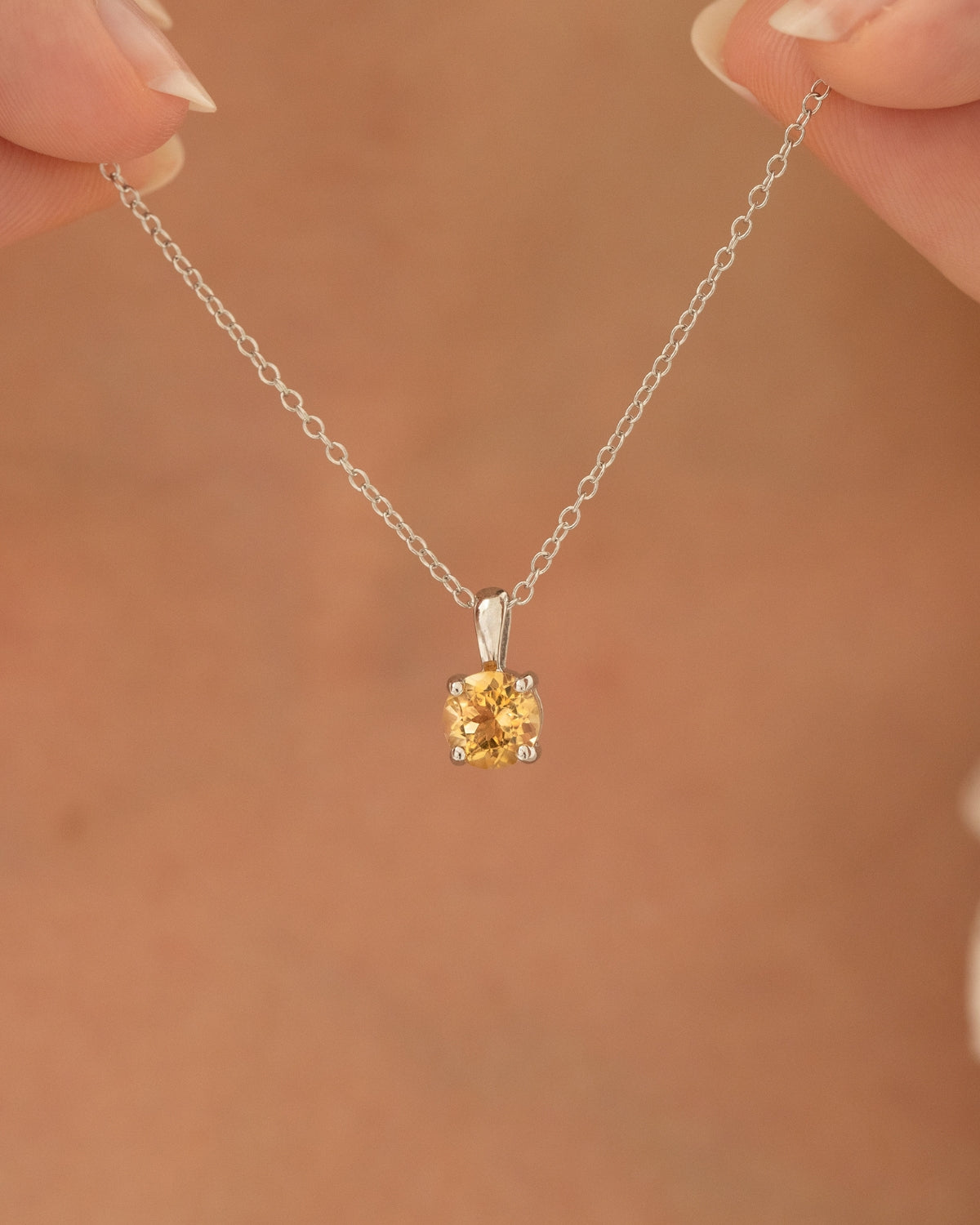 Silver necklace with a round citrine pendant held by hands against a brown background
