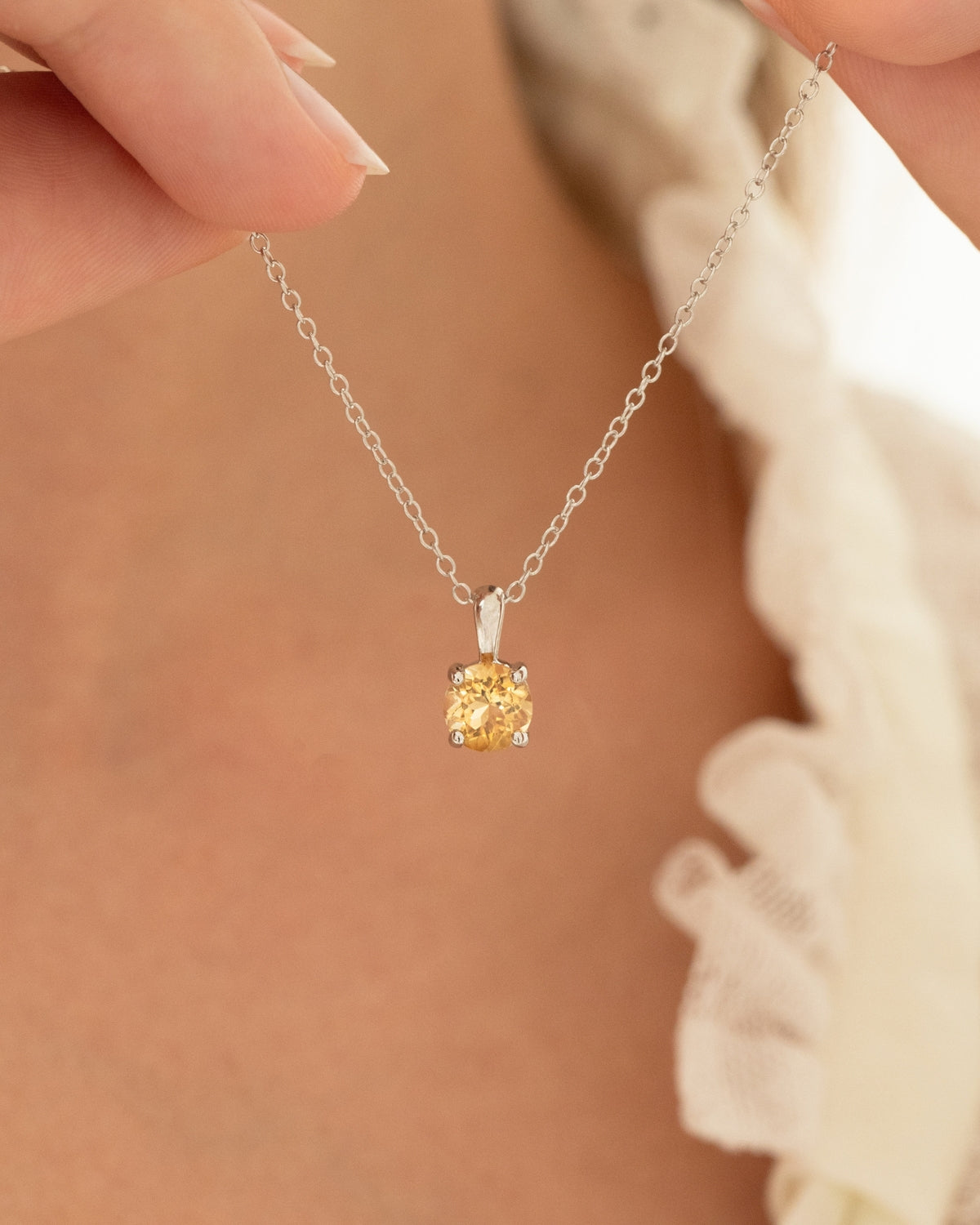 Silver necklace with a round citrine pendant held by a hand against a blurred background