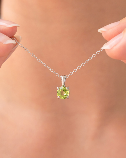 Silver necklace with a green peridot gemstone held by hands against a blurred background