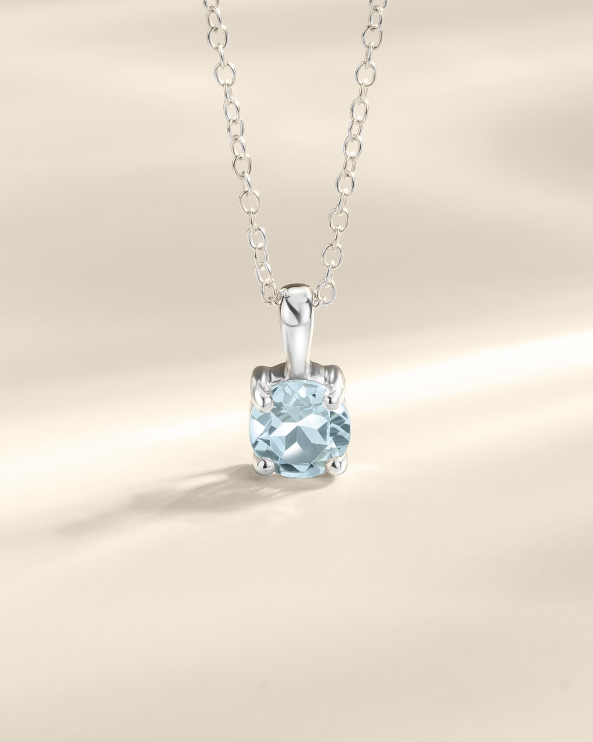 Silver necklace with a blue topaz gemstone pendant on a beige background