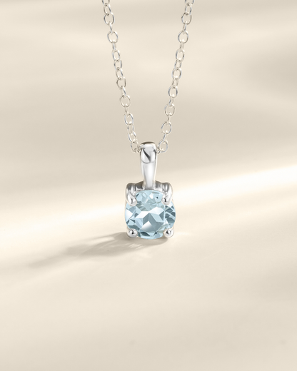 Silver necklace with a blue topaz gemstone pendant on a beige background