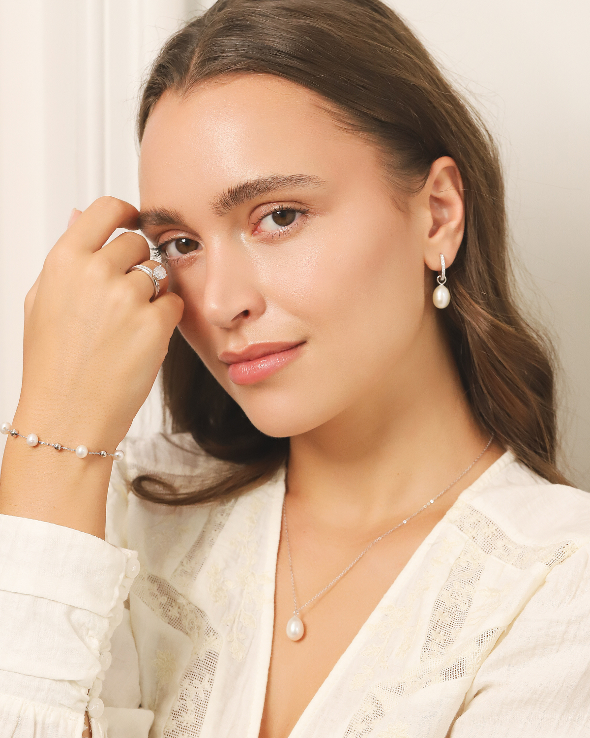 Woman wearing pearl silver jewellery including earrings, necklace, and bracelet against a neutral background
