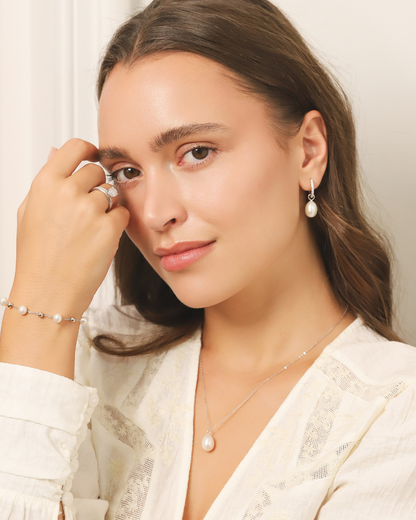 Woman wearing pearl silver jewellery including earrings, necklace, and bracelet against a neutral background