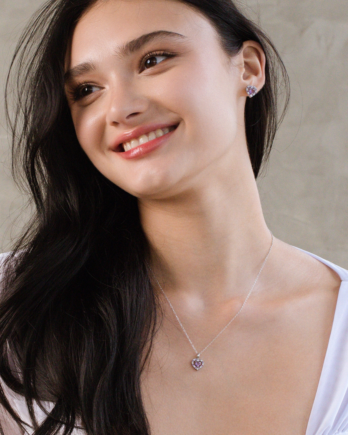 Woman wearing a silver amethyst necklace and earrings with a neutral background