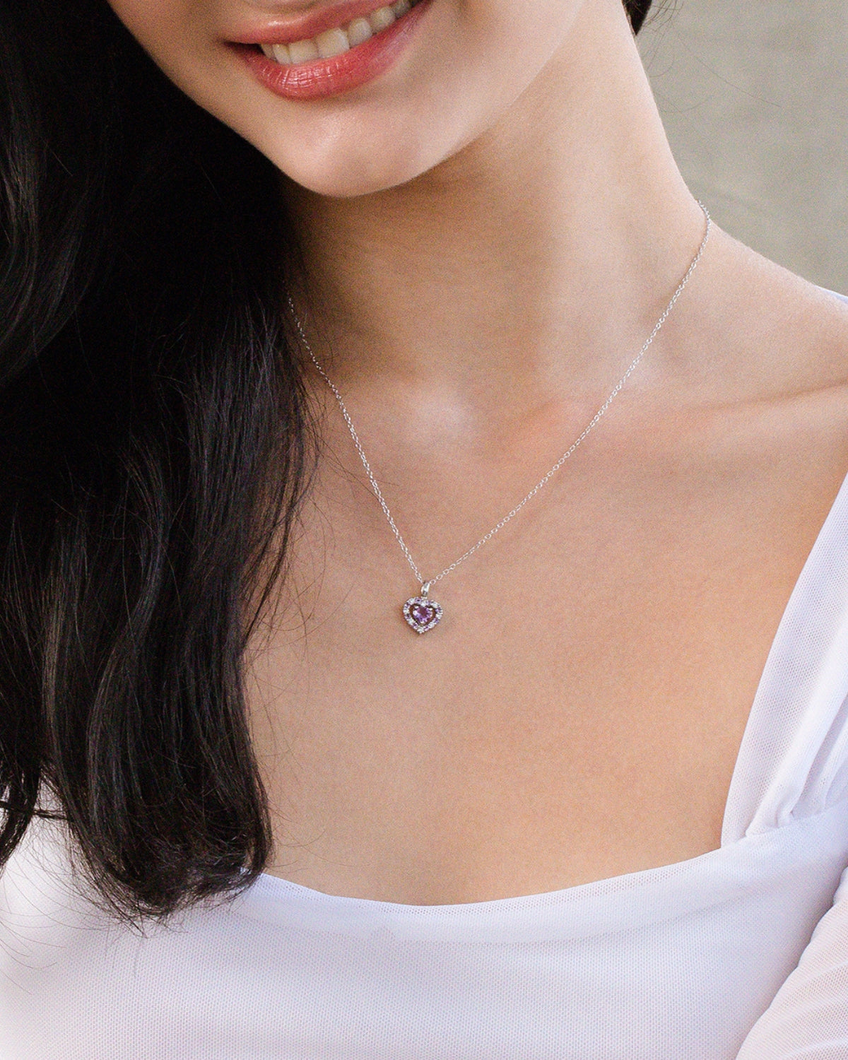 Woman wearing a silver necklace with a purple amethyst heart pendant.