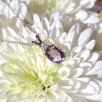 Silver necklace with a purple amethyst gemstone pendant on a white flower