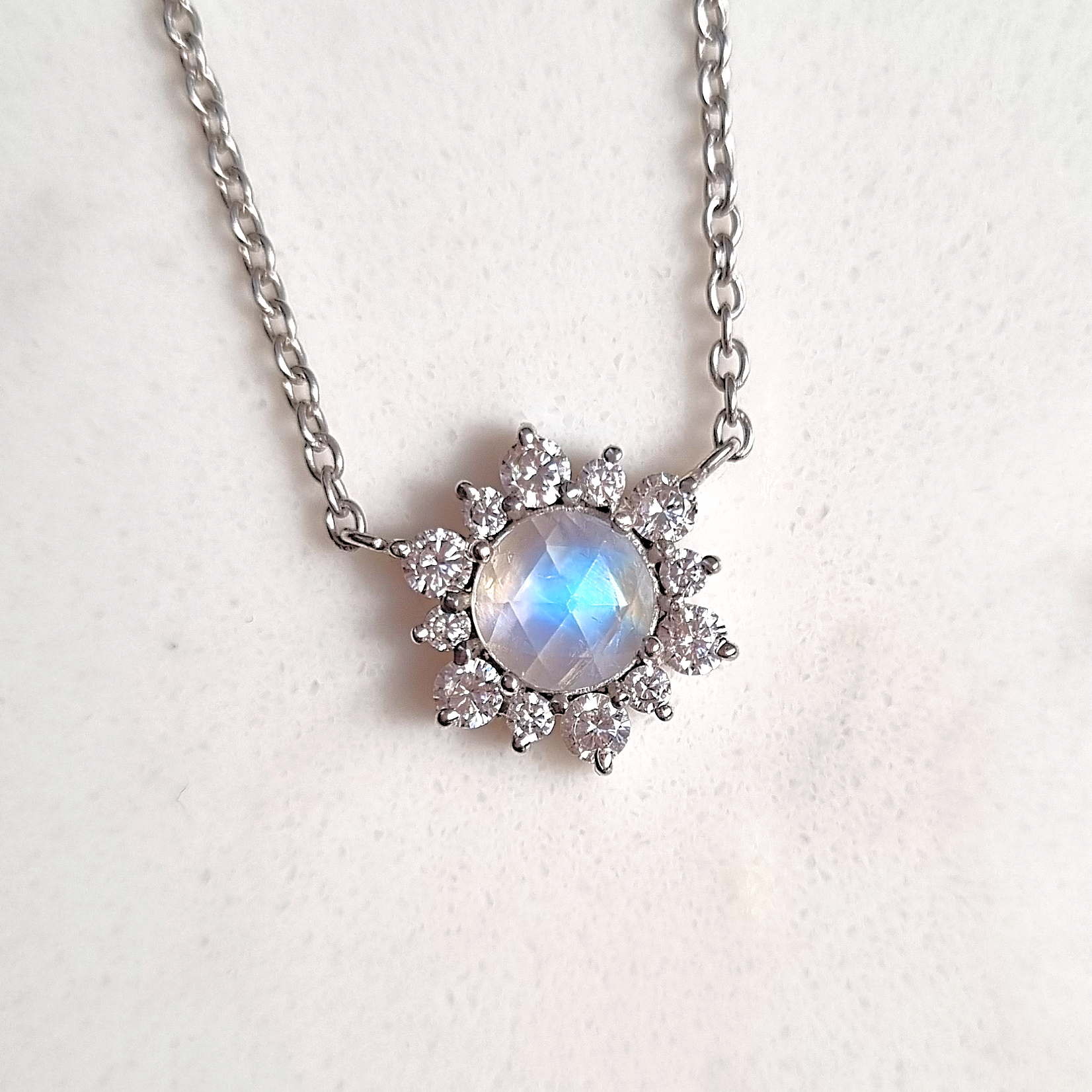 Silver necklace with a rainbow moonstone gemstone and smaller stones on a light background