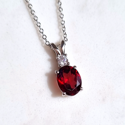 Silver necklace with a red garnet gemstone pendant on a white background
