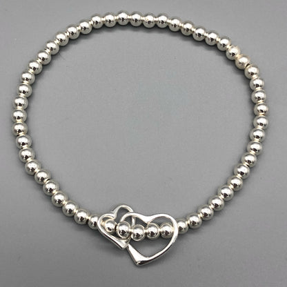 A sterling silver bracelet featuring a double interlinked open heart charm as the central element, with small silver beads on stretch elastic by My Silver Wish